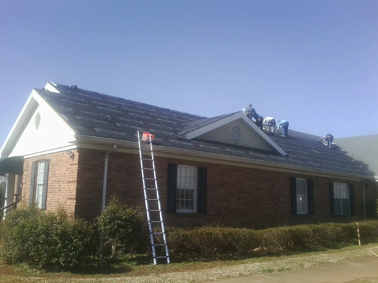 Crew tearing shingles off a brick ranch roof with a ladder set — Metal Roof Repair work by our crew in Ardsley
