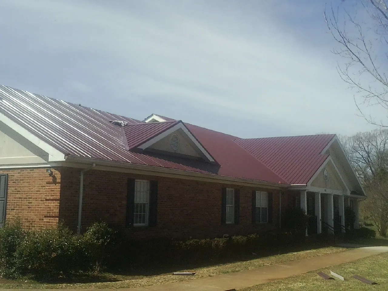 Red metal roof with gabled entries on a long brick building, from a Hail Damage Roof Repair job in Ardsley