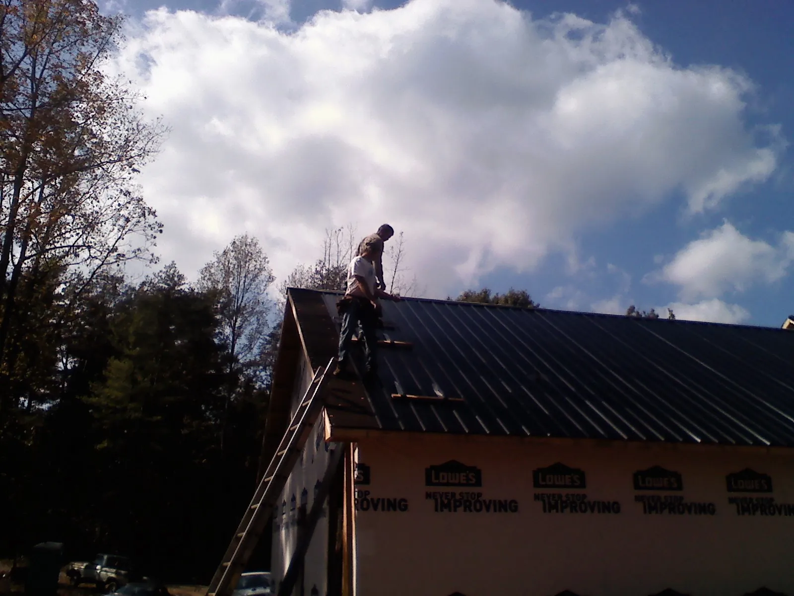 Roofer fastening dark metal panels high against a cloudy sky, from a Roof Inspection job in Ardsley